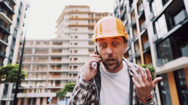 Mühendis telefonda konuşuyor. İnşaat alanında telefonu kullanan bir mimar. Foreman 'ın telefon kontrol işlemleri. İnşaat sektöründe inşaat işçisi iletişimi. Profesyonel telefon binası.