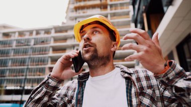 Mühendis telefonda konuşuyor. İnşaat alanında telefonu kullanan bir mimar. Foreman 'ın telefon kontrol işlemleri. İnşaat sektöründe inşaat işçisi iletişimi. Profesyonel telefon binası.