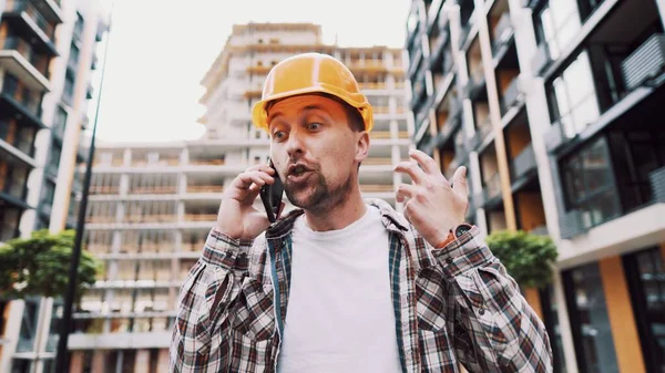 オレンジのハード帽子の怒っている男性建築家は 建設現場で電話で誓う 携帯電話で感情的に不満を交渉する再生シャツのビルダー 悲鳴を上げるストレス建築設計者 — ストック写真