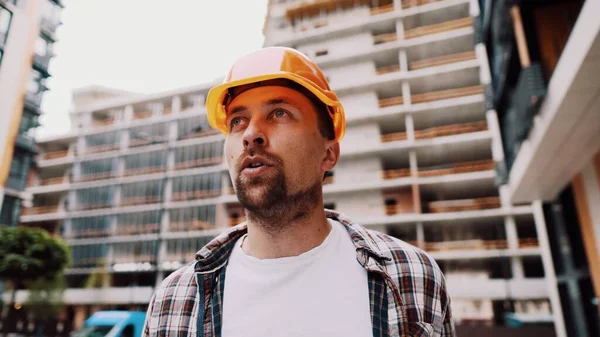 Angry builder, dissatisfied with deadline of work, swears at stress while talking to foreman on phone background of construction site. Wrathful architect, construction engineer talking on cell phone.