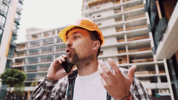 オレンジのハード帽子の怒っている男性建築家は 建設現場で電話で誓う 携帯電話で感情的に不満を交渉する再生シャツのビルダー 悲鳴を上げるストレス建築設計者 — ストック写真