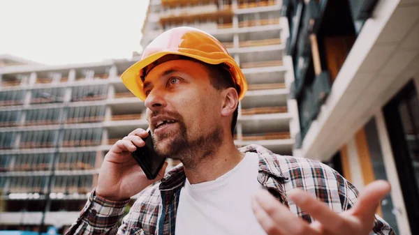 工事の締め切りに不満を持つ怒っているビルダーは 建設現場の電話背景でフォアマンと話をしながらストレスで身に着けています 携帯電話で話す建設技術者 — ストック写真