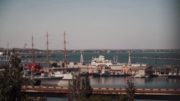 Uma vista de uma altura do porto de uma cidade à beira-mar em um dia ensolarado, onde navios de vários tamanhos e propósitos estão localizados, contra o pano de fundo de uma vista da cidade e edifícios. O tema do transporte marítimo — Vídeo de Stock