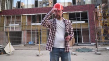 Beyaz erkek ustabaşı yorgun ve arka plandaki şantiyede kahve içiyor. Koruyucu ekipman mühendisi kahve molası. İnşaat müfettişi yorucu bir günden sonra sıcak içecek içiyor.