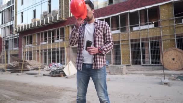 Инженер-строитель делает перерыв на кофе на стройке. Кавказский мужчина с кофейной чашкой на вынос и защитной экипировкой сломался во время работы на месте. Строитель пьет кофе — стоковое видео