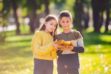 Kardeşler arasındaki dostluk. Kardeşler dışarıda, parlak renkli geçmişleri var. Çocukların sonbahar portresi. Erkek ve kız kardeş sonbahar park yapraklarında oynuyorlar. Aile aktif sonbahar hafta sonu konsepti.
