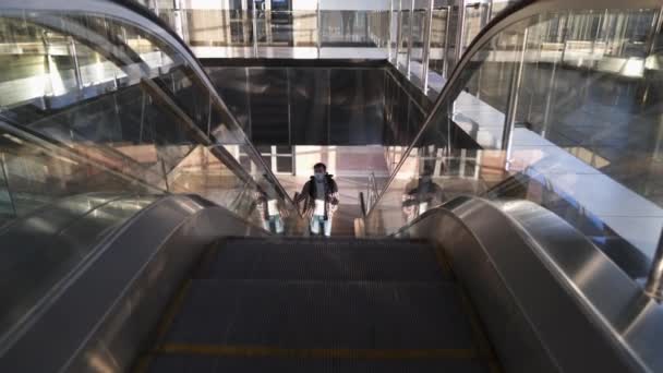 Pojištění na cestu. Kavkazský turista čelí masce s batohem na eskalátoru na letištním terminálu. Prevence pandemie koronaviru COVID-19 během cestování. Zůstaň v bezpečí. Nový normální — Stock video
