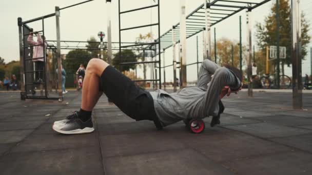 Pria kaukasia menggunakan pemijat roller busa untuk memijat dan mengendurkan otot setelah latihan di gym luar ruangan. Pijat jaringan dalam dengan Fisioterapi getaran Foam Roller. Sakit punggung — Stok Video