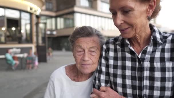 Sjuksköterska som tar hand om äldre. Frivilliga sjuksköterska kramar äldre kvinna, ler, är glad, promenader på gården. Begreppet pensionat, vårdhem, assistans till äldre. Gammal dotter besöker mormor — Stockvideo