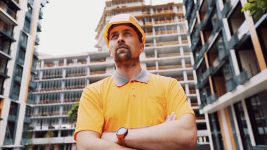 Gururla yapılmış bir portre. Kolları çapraz olan başarılı bir mimar ya da inşaatçı. İnşaat işçisi inşaat alanında kolları bağlı duruyor. Profesyonel bina yöneticisi..