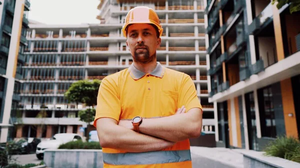 安全ヘルメットと建設現場で誇り高い表現でポーズオレンジ反射制服で交差腕を持つ若い白人建築家 建設現場で働く誇り高い労働者 労働者の肖像 — ストック写真