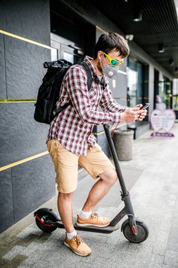 Koruyucu yüz maskesi takan erkek kurye, elektrikli scooterla teslimat adresine ulaştı. Çevre dostu taşımacılıkta hedef 19 sırasında teslim edildi. Büyük şehirde kirlilik. Başbakan 2.5 maskesi.