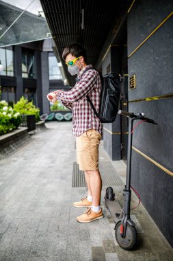 Koruyucu yüz maskesi takan erkek kurye, elektrikli scooterla teslimat adresine ulaştı. Çevre dostu taşımacılıkta hedef 19 sırasında teslim edildi. Büyük şehirde kirlilik. Başbakan 2.5 maskesi.