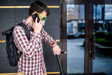 Koruyucu yüz maskesi takan erkek kurye, elektrikli scooterla teslimat adresine ulaştı. Çevre dostu taşımacılıkta hedef 19 sırasında teslim edildi. Büyük şehirde kirlilik. Başbakan 2.5 maskesi.