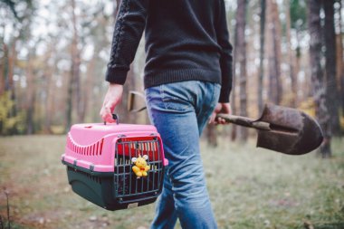 Yasadışı hayvan gömme teması. Ormanda self-servis hayvan mezarı. İnsan, yanında ölü kedi ya da köpek ve ormana gömmek için büyük bir kürek taşıyan taşıyıcı taşır. RIP evcil hayvan.