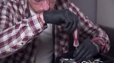 Genç bir adam evde kendi mutfak aletlerini tamir etmeye çalışıyor, bir kahve makinesi. Beyaz erkek, ekose gömlek, güvenlik gözlüğü ve eldiven takmış bir tornavidayla kahve makinesini tamir ediyor.