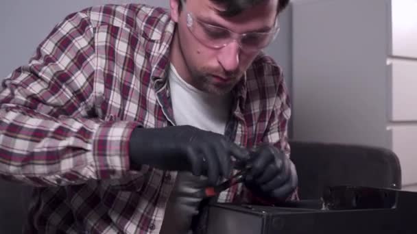 Un joven está tratando de arreglar sus propios electrodomésticos en casa, una cafetera. Hombre caucásico repara una máquina de café con un destornillador vestido con una camisa a cuadros y gafas de seguridad y guantes — Vídeo de stock