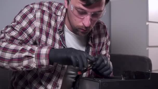 Молодой человек пытается починить собственную кухонную технику дома, кофеварку. Кавказский мужчина ремонтирует кофеварку с отвёрткой, одетой в клетчатую рубашку и защитные очки и перчатки — стоковое видео