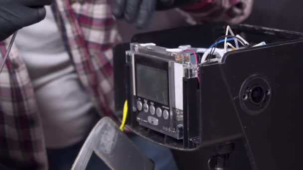 Een jongeman probeert zijn eigen keukenapparatuur thuis te maken, een koffiezetapparaat. Blanke man repareert een koffiemachine met een schroevendraaier gekleed in een geruit shirt en veiligheidsbril en handschoenen — Stockvideo