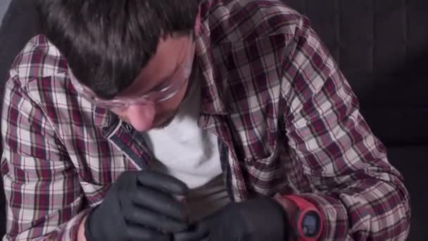 Молодой человек пытается починить собственную кухонную технику дома, кофеварку. Кавказский мужчина ремонтирует кофеварку с отвёрткой, одетой в клетчатую рубашку и защитные очки и перчатки — стоковое видео