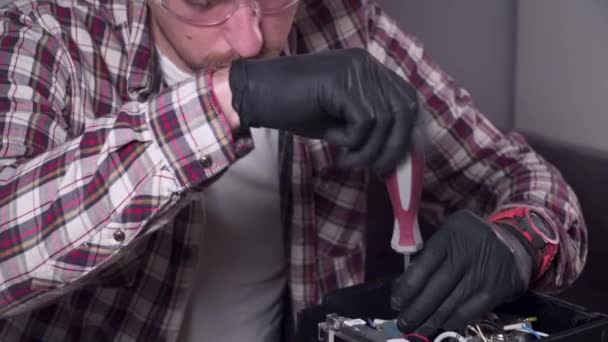 A young man is trying to fix his own kitchen appliances at home, a coffee maker. Caucasian male repairs a coffee machine with a screwdriver dressed in a plaid shirt and safety glasses and gloves — Stock Video