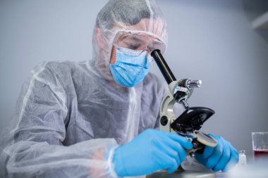 Kimya laboratuvarında mikroskoptan bakan beyaz koruyucu giysili bir tıbbi uzman. Aşı koronavirüsü arayın. Covid 19 uyuşturucu icadı. Laboratuvar bilim adamları ilaç ürünleri üretiyor