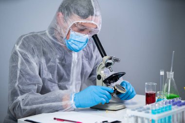 İlaç üreticileri en iyi bileşeni icat ederek viral ilaçlar geliştiriyorlar. Yüz maskeli kişisel koruyucu ekipman takan bilim adamları laboratuarda mikroskop altında hücre sonuçlarını izliyorlar.