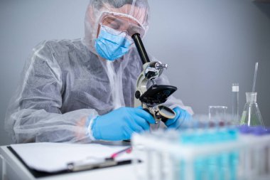 Kimya laboratuvarında mikroskoptan bakan beyaz koruyucu giysili bir tıbbi uzman. Aşı koronavirüsü arayın. Covid 19 uyuşturucu icadı. Laboratuvar bilim adamları ilaç ürünleri üretiyor