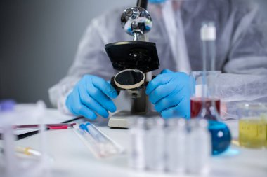 Kimya laboratuvarında mikroskoptan bakan beyaz koruyucu giysili bir tıbbi uzman. Aşı koronavirüsü arayın. Covid 19 uyuşturucu icadı. Laboratuvar bilim adamları ilaç ürünleri üretiyor