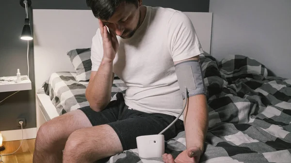 Young man measuring blood pressure at home. Hypertensive patient performing an automatic blood pressure test. Doing my regular checkup. High blood pressure hypertension disease. Automatic tonometer.