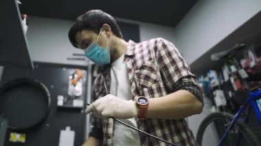 Bisiklet tamircisi Coronavirus salgını sırasında karantina standartlarına uygun olarak bisiklet tamir eder ve bakımını yapar. Tıbbi maske ve eldiven takar. Covid 19 'u kilitlerken bireysel taşıma