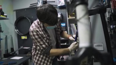 Tamirci atölyede bisiklet tamir ediyordu. Tıbbi maske takıyordu. Korunaklı yüz maskesi takan karantina altındaki koronavirüs salgınında insan bisikleti tamir edilir. İnsan döngüyü inceler ve düzeltir. Spor mağazası konsepti