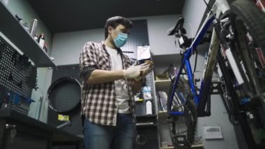 Koronavirüs salgını sırasında bisiklet mağazasında tema hizmeti bakım ve onarım. Tamirci koruyucu maske takarak dağ bisikletini tamir ediyor, yeni kurallar covid 19. Konu işçi mesleği