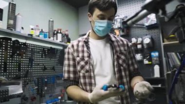 Tamirci atölyede bisiklet tamir ediyordu. Tıbbi maske takıyordu. Korunaklı yüz maskesi takan karantina altındaki koronavirüs salgınında insan bisikleti tamir edilir. İnsan döngüyü inceler ve düzeltir. Spor mağazası konsepti