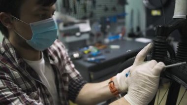 Bisiklet tamircisi Coronavirus salgını sırasında karantina standartlarına uygun olarak bisiklet tamir eder ve bakımını yapar. Tıbbi maske ve eldiven takar. Covid 19 'u kilitlerken bireysel taşıma