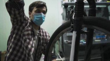 Bisiklet tamircisi Coronavirus salgını sırasında karantina standartlarına uygun olarak bisiklet tamir eder ve bakımını yapar. Tıbbi maske ve eldiven takar. Covid 19 'u kilitlerken bireysel taşıma