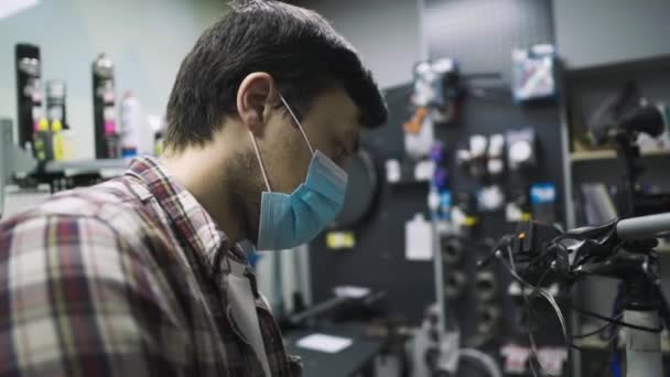 Servizio a tema manutenzione e riparazione di biciclette nel negozio di biciclette durante l'epidemia di coronavirus. Riparazioni meccaniche ciclo montano indossando maschera protettiva, nuove regole covid 19. Professione di operaio soggetto — Video Stock