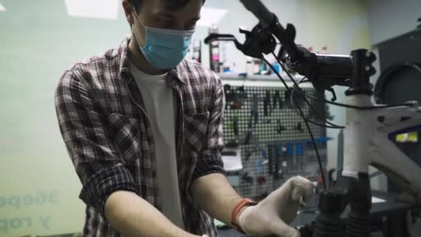 Service engineer voert diagnostiek en reparaties op de fiets in professionele werkplaats, het dragen van beschermende masker en veiligheidshandschoenen van klant covid 19. Onderwerp van de dienst tijdens de coronaviruspandemie — Stockvideo