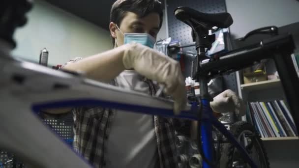 Ingeniero de servicio realiza diagnósticos y reparaciones en bicicleta en taller profesional, usando máscara protectora y guantes de seguridad del cliente covid 19. Tema de servicio durante la pandemia de coronavirus — Vídeo de stock