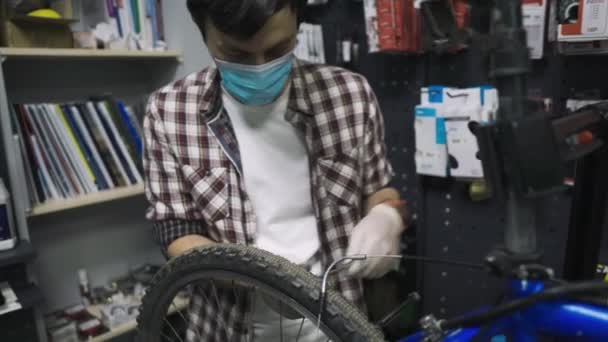 Θεματική συντήρηση και επισκευή ποδηλάτων σε κατάστημα ποδηλάτων κατά τη διάρκεια επιδημίας κορωναϊού. Μηχανικός επισκευάζει ποδήλατο βουνού φορώντας προστατευτική μάσκα, νέοι κανόνες covid 19. Υποκείμενο επάγγελμα του εργάτη — Αρχείο Βίντεο