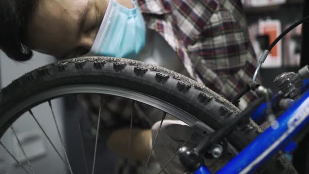 El mecánico de bicicletas repara y mantiene la bicicleta del cliente de acuerdo con los estándares de cuarentena durante la pandemia de coronavirus, usa máscara médica y guantes. Transporte individual durante el bloqueo covid 19 — Vídeo de stock