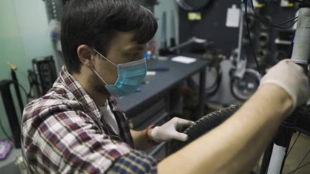Inżynier serwisu wykonuje diagnostykę i naprawy rowerów w profesjonalnym warsztacie, nosząc maskę ochronną i rękawice ochronne klienta covid 19. Temat serwisu podczas pandemii koronawirusowej — Wideo stockowe