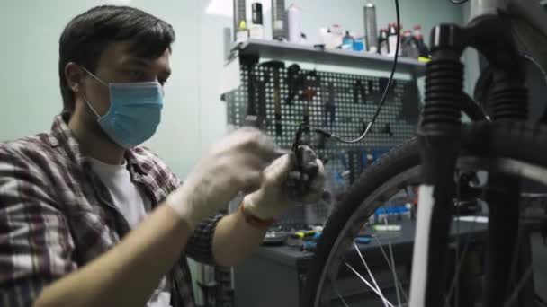 Tema service underhåll och reparation av cykel i cykelaffär under coronavirus epidemi. Mekaniker reparerar mountainbike bär skyddsmask, nya regler covid 19. Angående: Arbetaryrket — Stockvideo