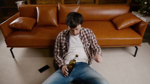 Mladý muž v depresi pije alkohol doma. Nezaměstnaný muž, opilý a pokračuje v pití lahve vína přímo na gauči u vánočního stromku. Závislost, osamělost, nervové zhroucení Nový rok dovolená — Stock video