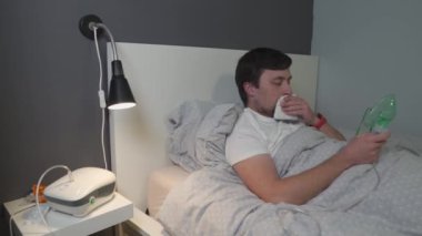 Koronavirüslü bir adam, yatakta kompresör nebulizer ilaç solunum maskesi kullanan bir grip. Solunum tıbbı. Astım tedavisi. Bronşit, astımlı sağlık ekipmanları. Alternatif tedavi
