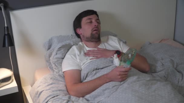 Koronavirüslü bir adam, yatakta nebulizör ilaç solunum maskesi kullanan bir grip. Solunum tıbbı. Astım tedavisi. Bronşit, astımlı sağlık ekipmanları. Alternatif ev tedavileri — Stok video