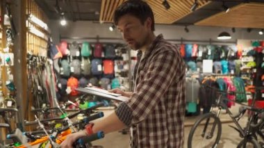 Satış asistanı alışveriş yapan kişiye spor malzemeleri mağazasında bisiklet seçmesinde yardımcı olur. Bisiklet dükkânı çalışanı müşteriye tavsiyede bulunur. Erkek bisikletçi kamerada bisikletlerden bahsediyor. Adam bisiklet hakkındaki video günlüğünü yönetiyor