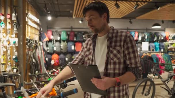 Jovem vendedor masculino caucasiano segurando apresentação de bicicletas mercadorias ao comprador, visão em primeira pessoa, loja profissional de artigos de viagem esportiva. Compra de equipamentos e serviço de qualidade de profissionais — Vídeo de Stock