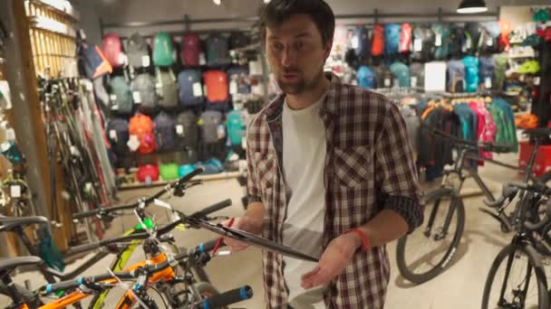 Verkäuferin hilft Shopper bei der Fahrradauswahl im Sportartikelgeschäft. Fahrradverkäuferin berät Kunden. Männliche Fahrradverkäufer sprechen vor laufender Kamera über Fahrräder. Mann führt Videoblog über Radfahren — Stockvideo