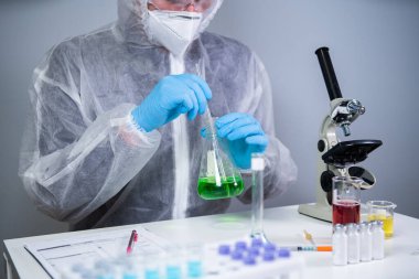 Bilim adamı yeşil sıvıyı kabın içinde sallıyor. Laboratuvarda test ya da araştırma yapan genç bir laboratuvar asistanı. Teknisyen kimya laboratuarı deneyini test ediyor ve mikroskop ile birlikte cam tüpü sallıyor..